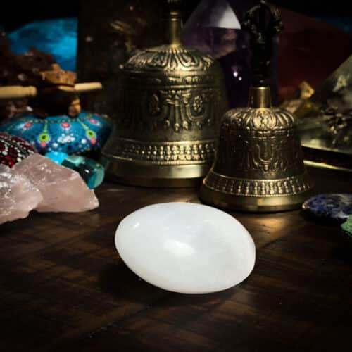 Selenite Palm Stone with bells behind it on a wooden table at the om shoppe