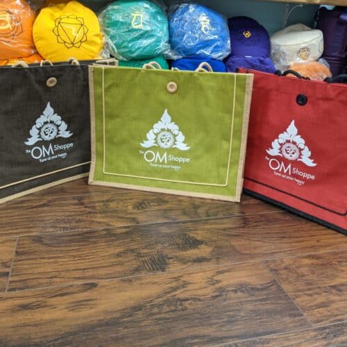 three jute tote bags with the om shoppe logo on them brown, green and red